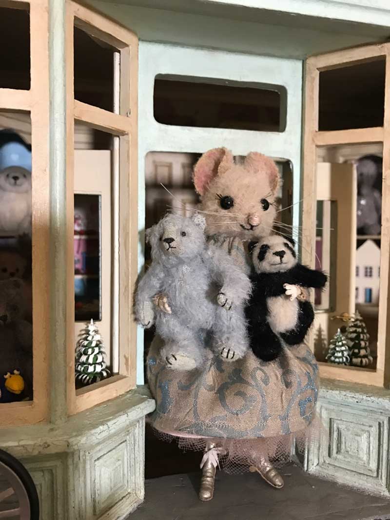 Marietta outside her toyshop, holding handsewn teddy bears. The shop is 1/12 scale.
